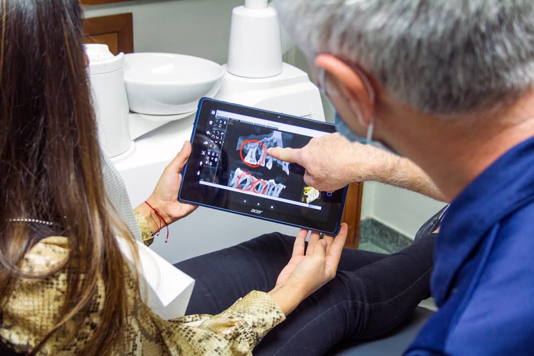 A dental hygienist reviewing patient records on a tablet while a modern operatory with digital displays glows in the background