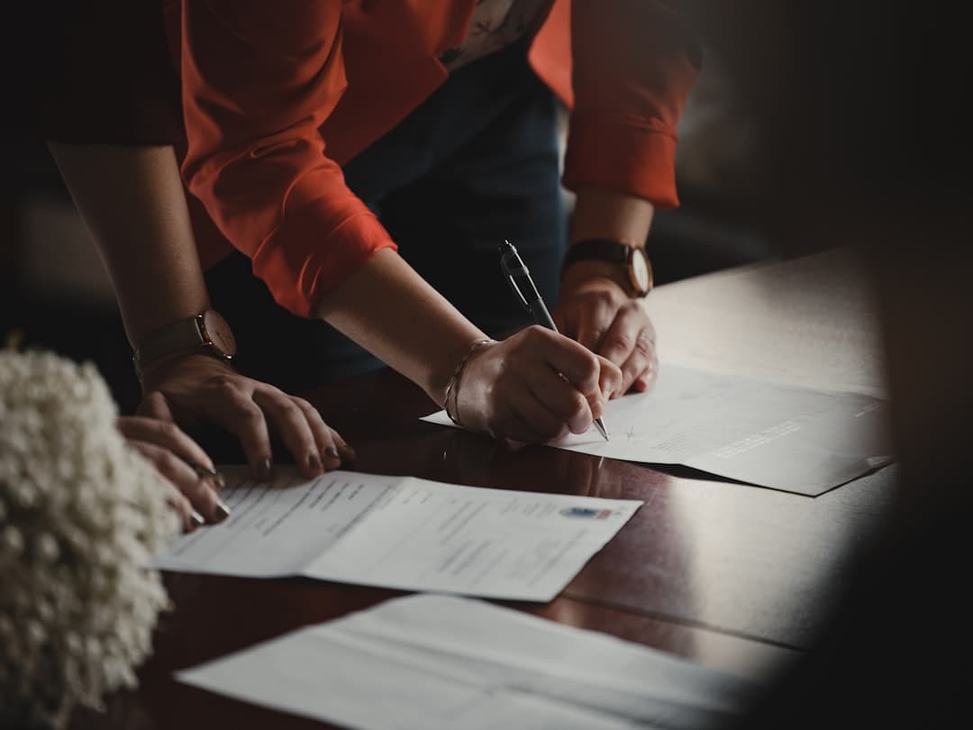 hands signing stacks of paperwork at a wooden desk, closing day for somebody