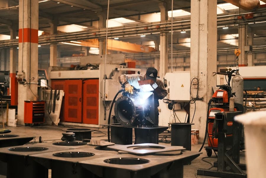 A welder in a fabrication shop with finished steel parts staged in the foreground