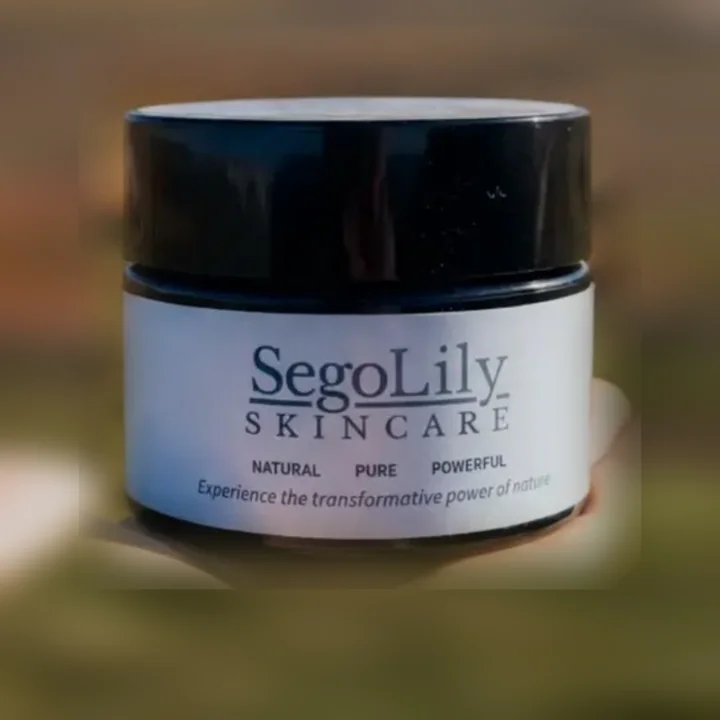 A jar of Sego Lily Skincare tallow balm held up over a Montana field