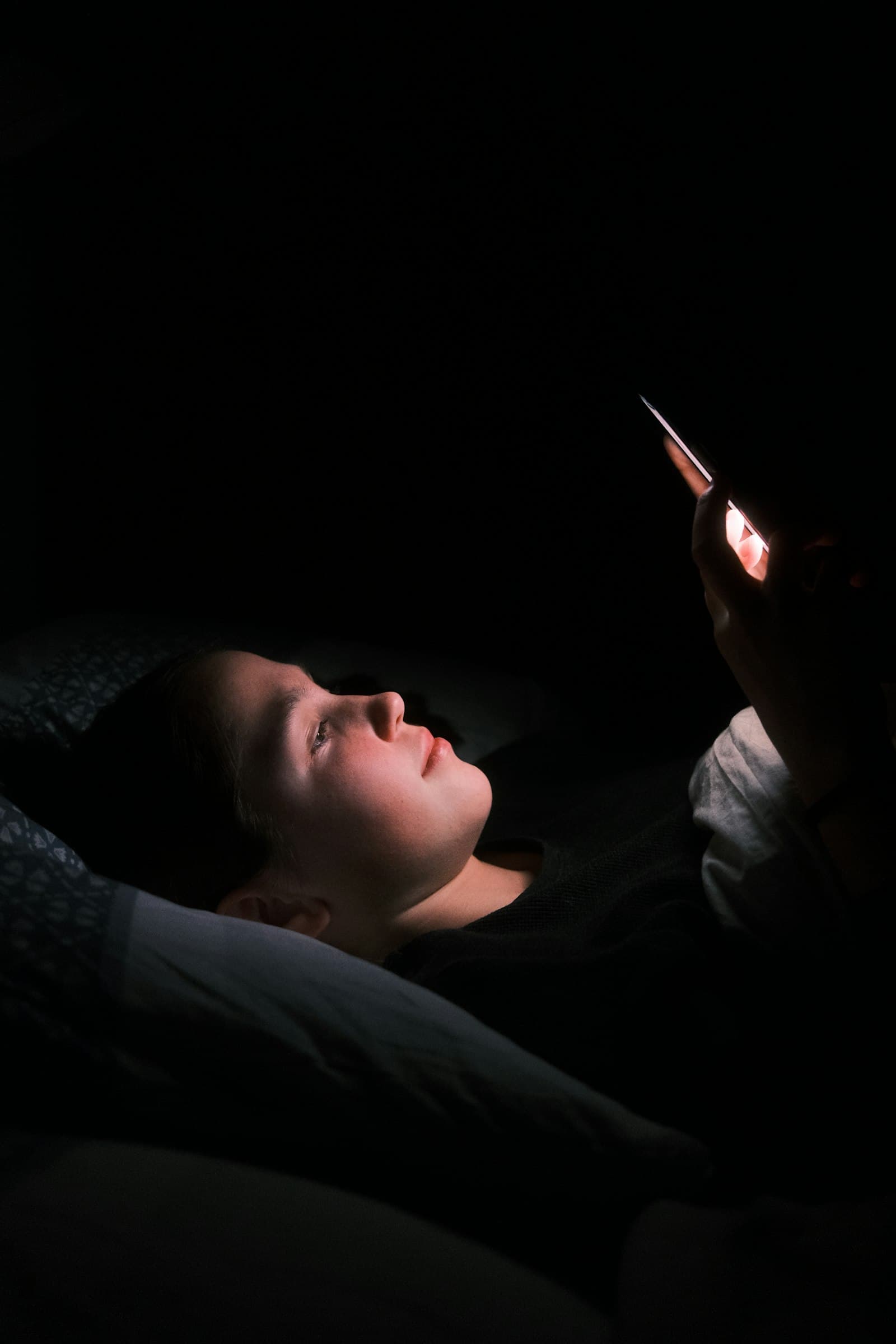 woman in bed at night lit by her glowing phone, deciding which HVAC company picks up first