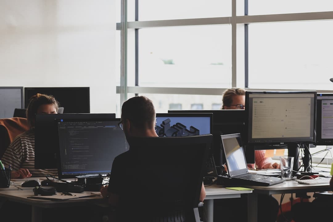 Office workers at dual monitor desks near tall windows, insurance producers quoting warm inquiries