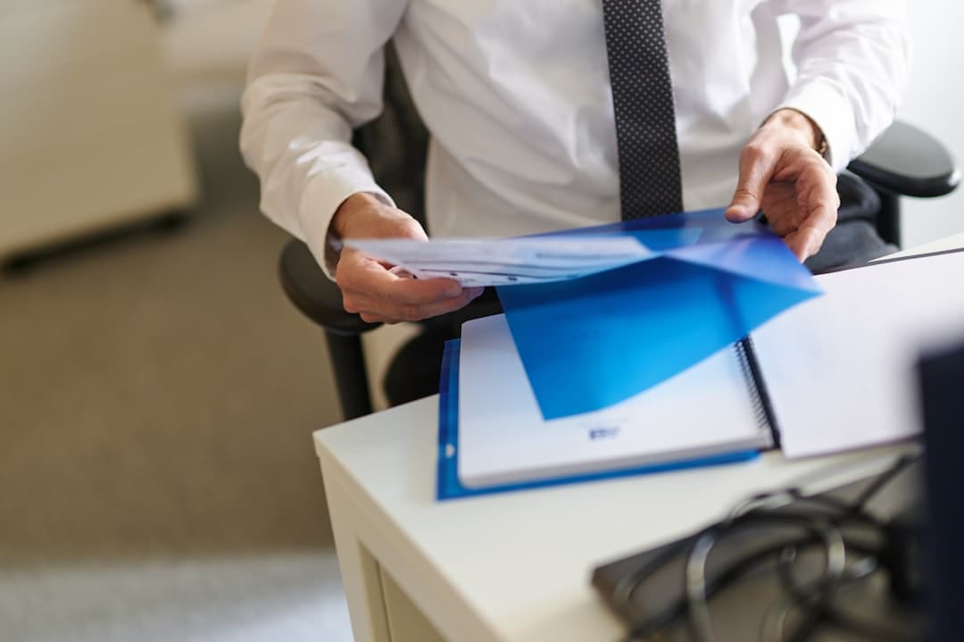 Man in white shirt holding blue document folder at desk, home insurance policy bound