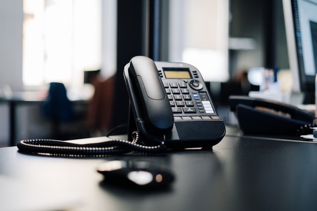 Black desk phone on dark office surface, the after-hours plumbing call just landed