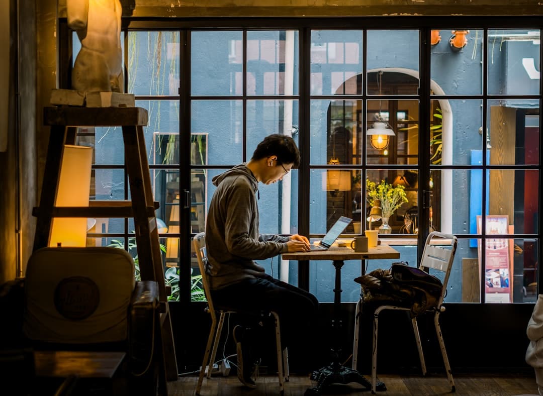 Freelancer at a cafe laptop reviewing Google Ads management costs, phone face down as usual