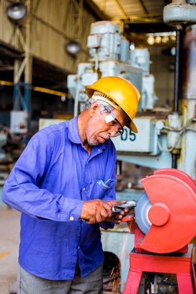 A machinist finishing a metal part on a bench grinder in a manufacturing workshop