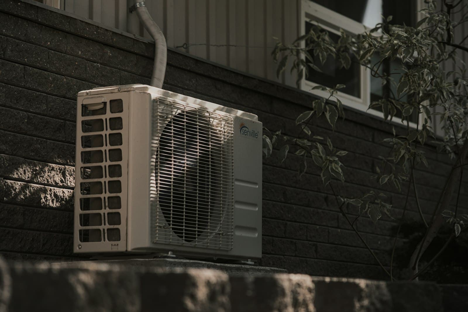 White AC condenser beside a brick house, the unit a past customer hasn't had serviced in two years