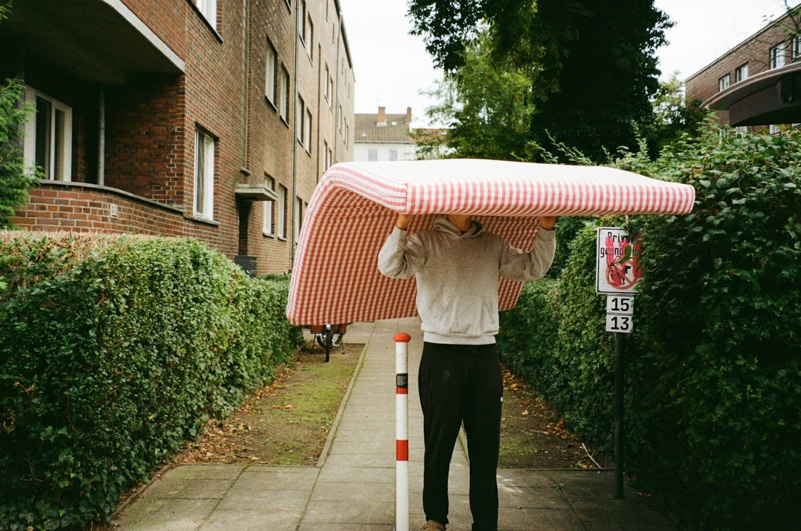 Man carrying an old striped mattress down the sidewalk, the haul-away nobody wants to do twice
