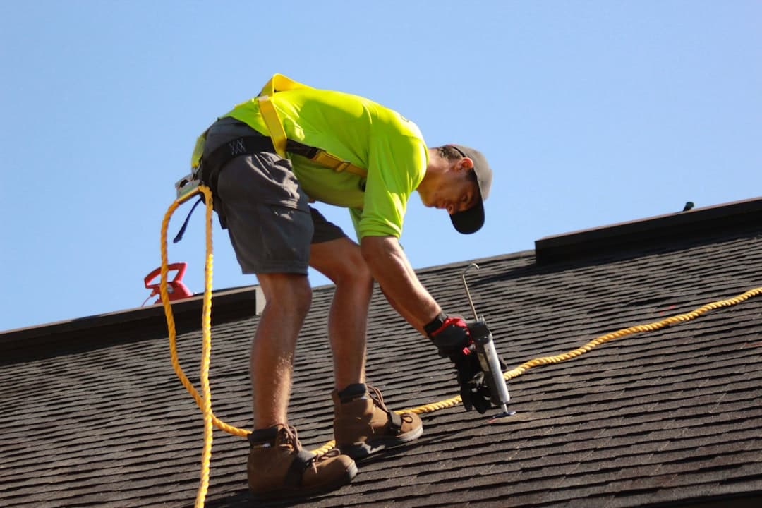 Roofer using a nail gun on a shingled roof
